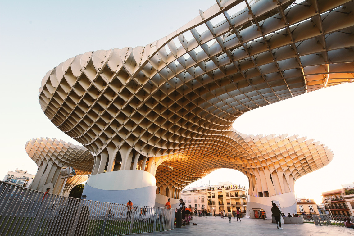The sweeping wooden lattice of Setas de Sevilla, also known as Metropol Parasol, rises above Plaza de la Encarnaci&oacute;n in Seville, Spain. Pedestrians walk beneath the curved structure in the warm evening light.