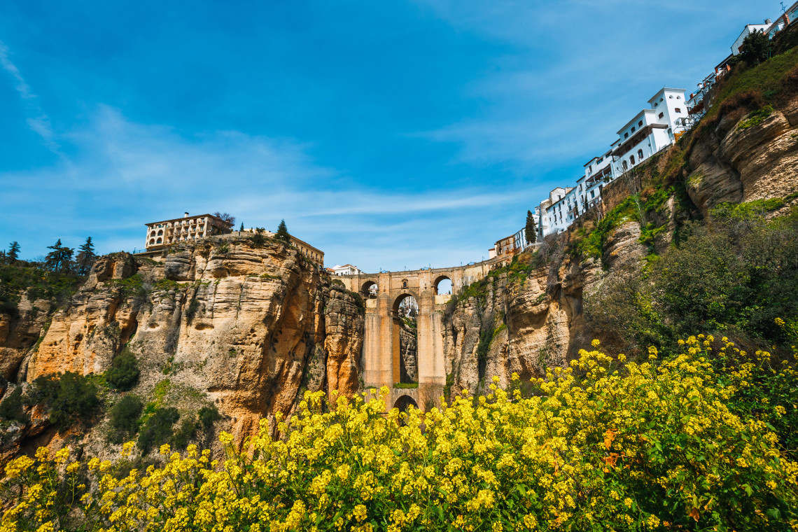 Puente Nuevo connects the two sides of Ronda, Spain, across the steep rocky walls of El Tajo Gorge. White buildings line the cliff above the monumental stone bridge.