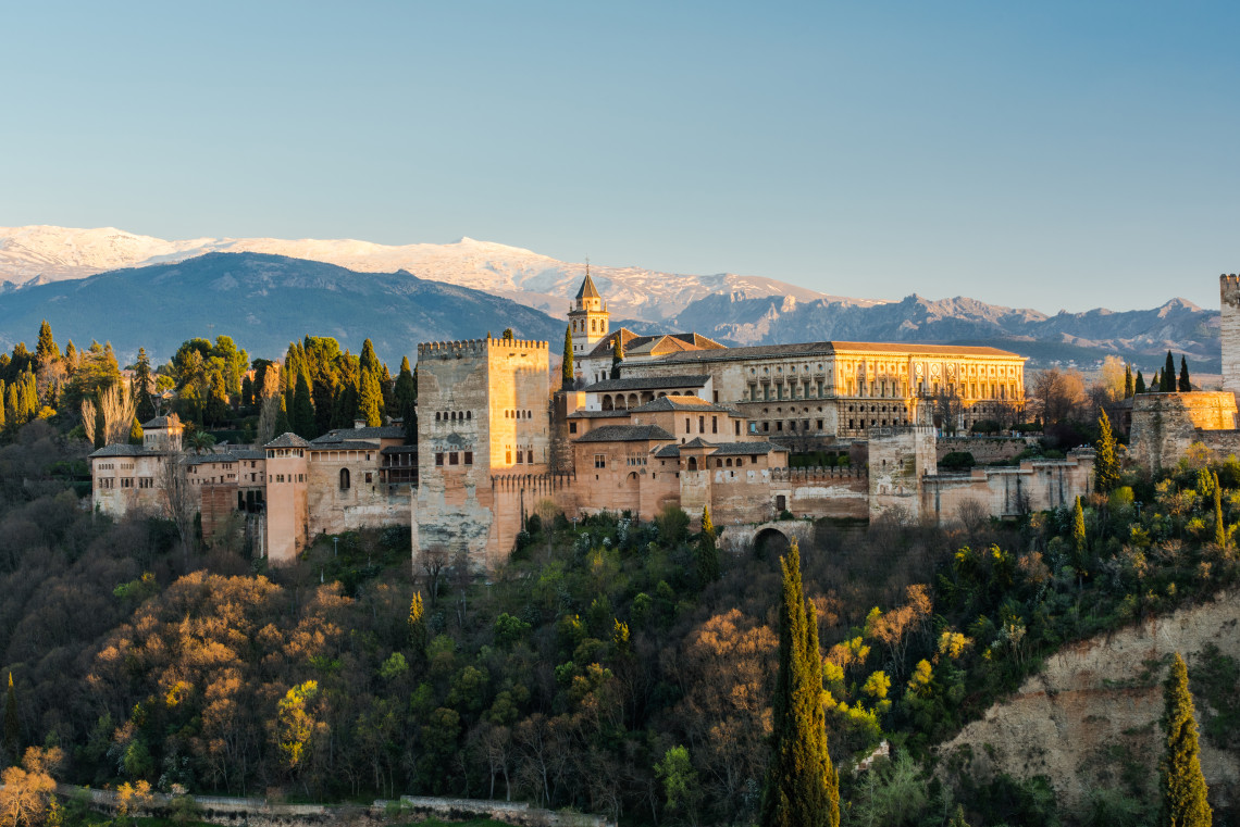 Alhambra palace complex in Granada glowing at sunset with snow-capped Sierra Nevada mountains behind