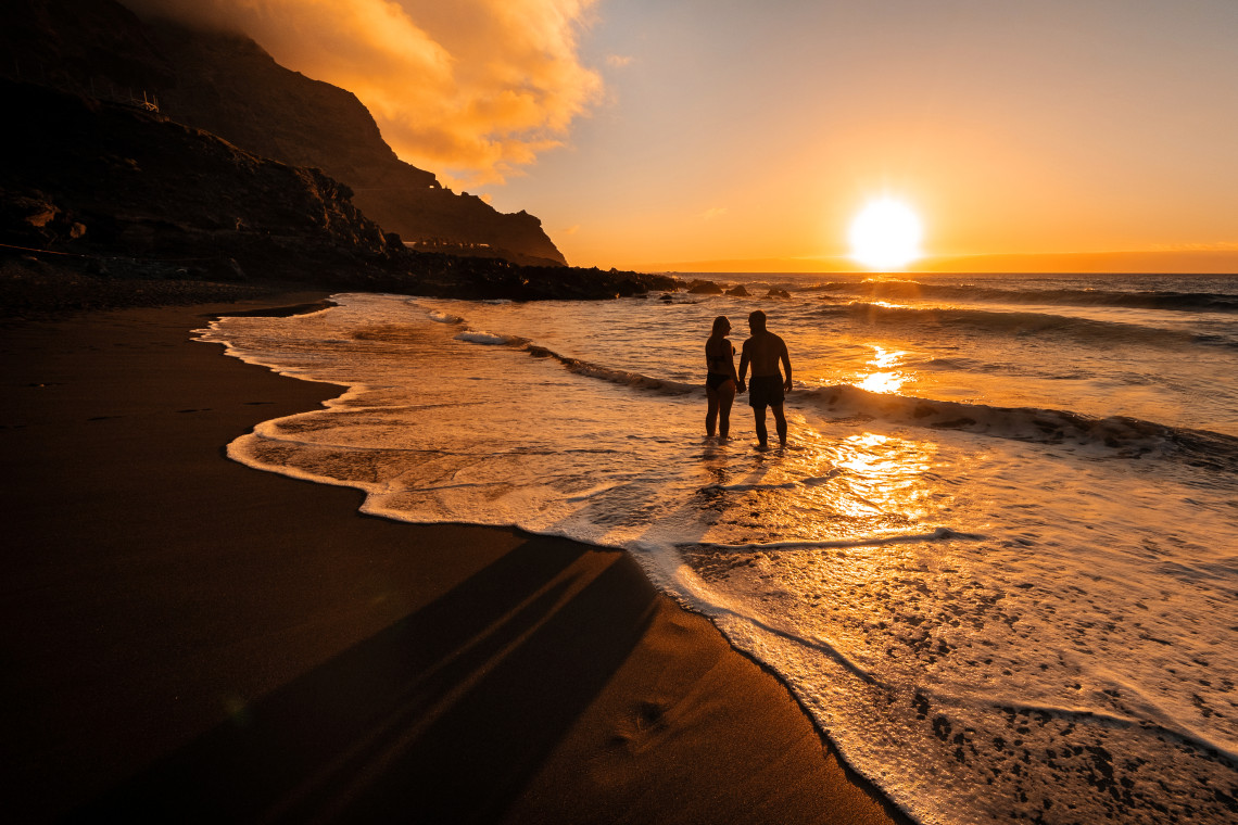 Silhouette of a couple standing in the surf at sunset on a Tenerife beach, volcanic cliffs in the background