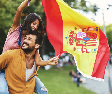 Couple celebrating outdoors with a large Spanish flag during a festival in Spain