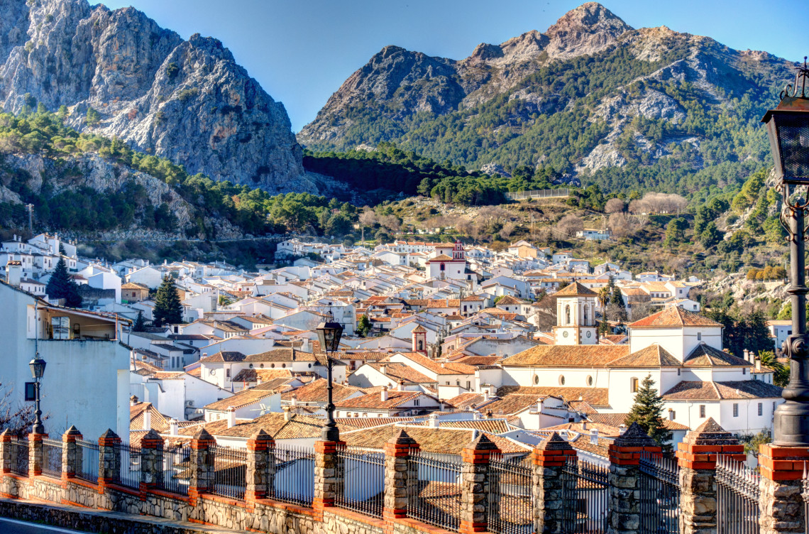 Whitewashed houses and tiled rooftops spread across Grazalema in C&aacute;diz, Spain, beneath the limestone mountains of the Sierra de Grazalema. A church tower rises near the centre of the compact Andalusian village.