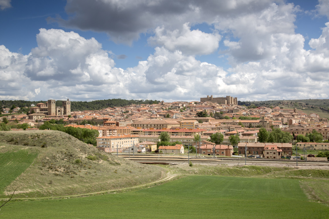 A panoramic view shows Sig&uuml;enza in Guadalajara, Spain, spreading across the hills beneath large clouds. The twin towers of Sig&uuml;enza Cathedral and the medieval castle rise above the terracotta rooftops.