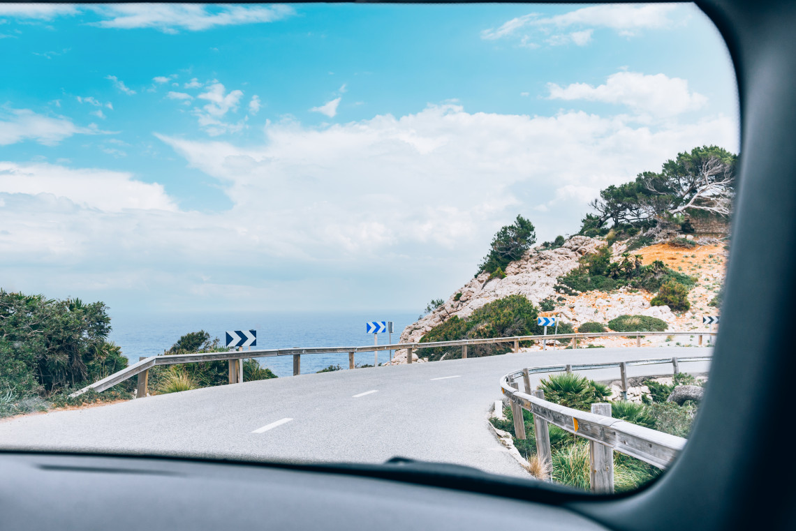 View through a car windscreen of a winding road near Cap de Formentor in Pollen&ccedil;a, Spain. The route curves around a rocky hillside overlooking the Mediterranean Sea on Mallorca.