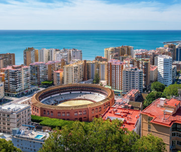 Aerial view of La Malagueta Bullring in Málaga, Spain, surrounded by residential buildings near the Mediterranean waterfront. The circular arena stands prominently against the city’s coastal skyline.