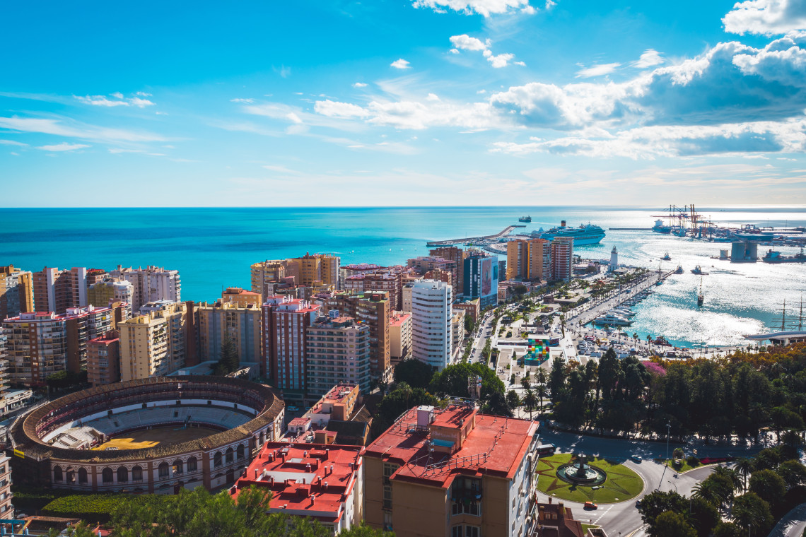 Panoramic view of M&aacute;laga, Spain, showing La Malagueta Bullring, residential buildings, the city port and the Mediterranean Sea. Cruise ships and marina facilities are visible along the waterfront.