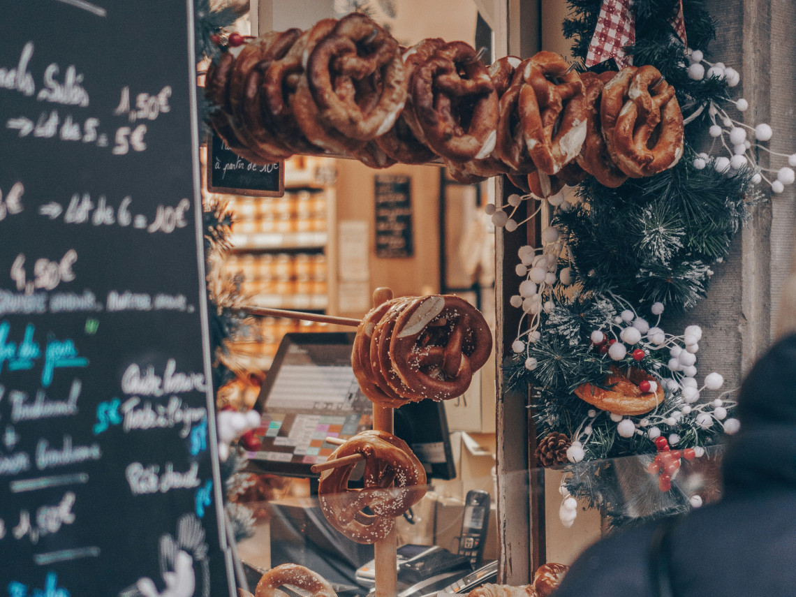 Traditional soft pretzels hang from a food stall decorated with evergreen garlands at a Christmas market in Strasbourg, France.