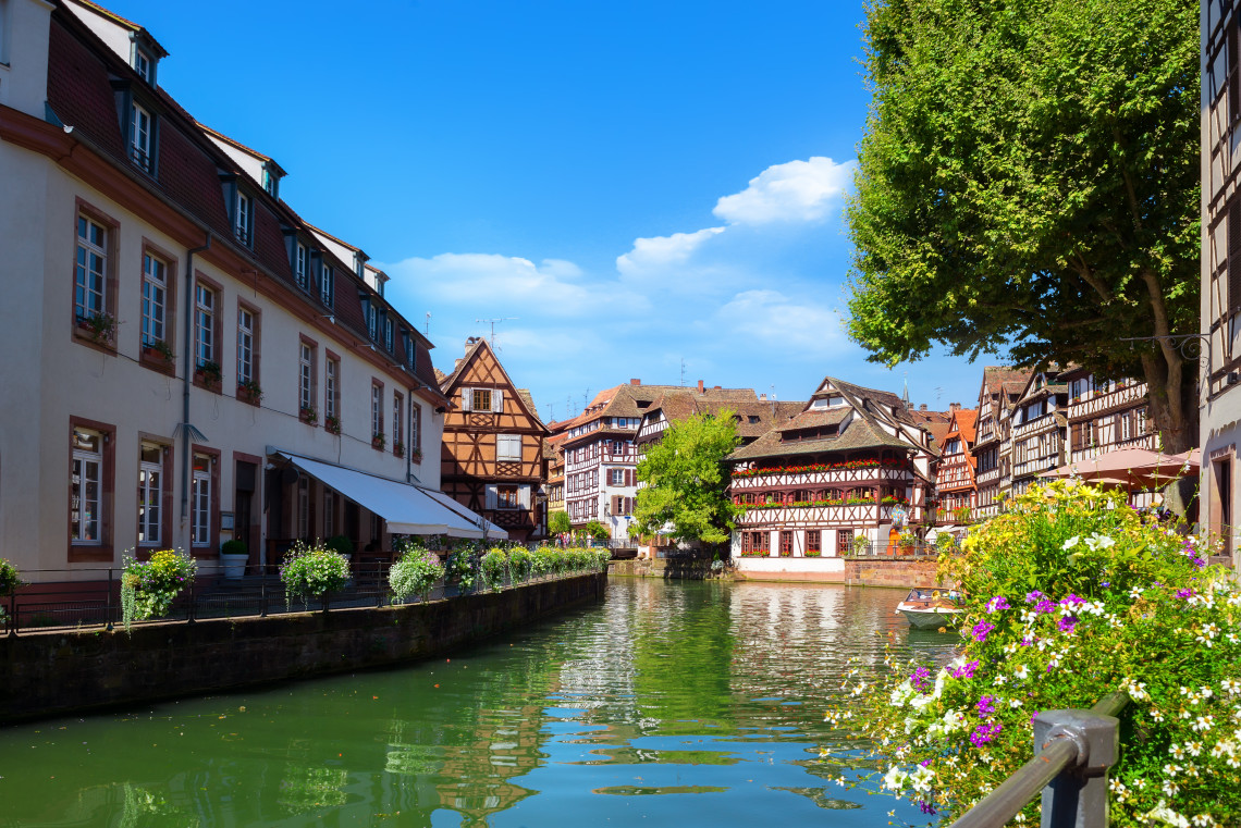 Daytime view of the Petite France district in Strasbourg, France, with half-timbered houses, flower-lined walkways and calm canal water.