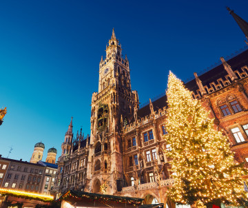 A large illuminated Christmas tree stands beside Munich’s New Town Hall at Marienplatz Christmas Market in Munich, Germany. The Gothic Revival clock tower rises above the festive square beneath a clear evening sky.