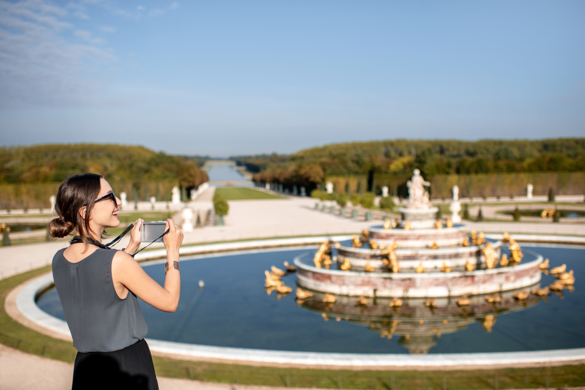 Woman tourist walking through the formal gardens of the Palace of Versailles, France