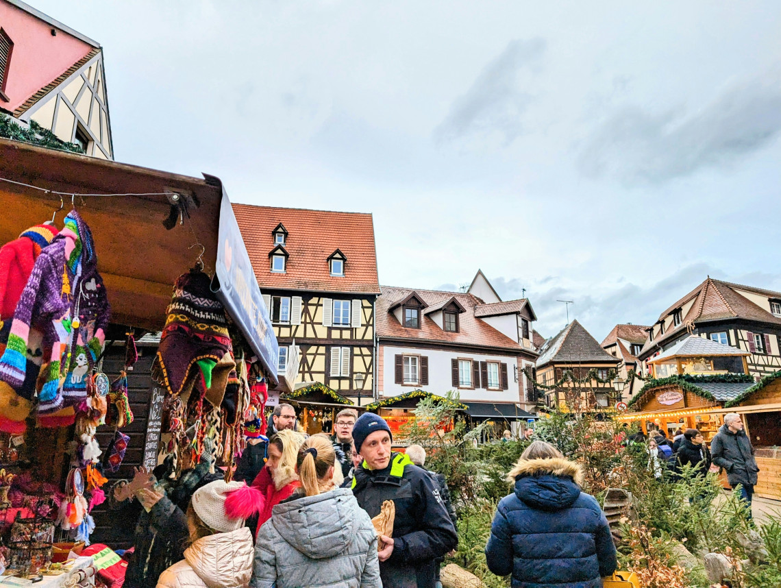 Crowded Christmas market with colorful craft stalls and half-timbered buildings in a traditional Alsatian village, France
