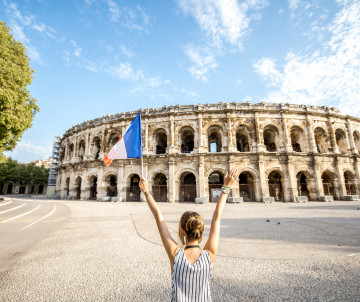 Woman holding a French flag with arms raised in front of the Roman amphitheater Arena of Nimes, southern France