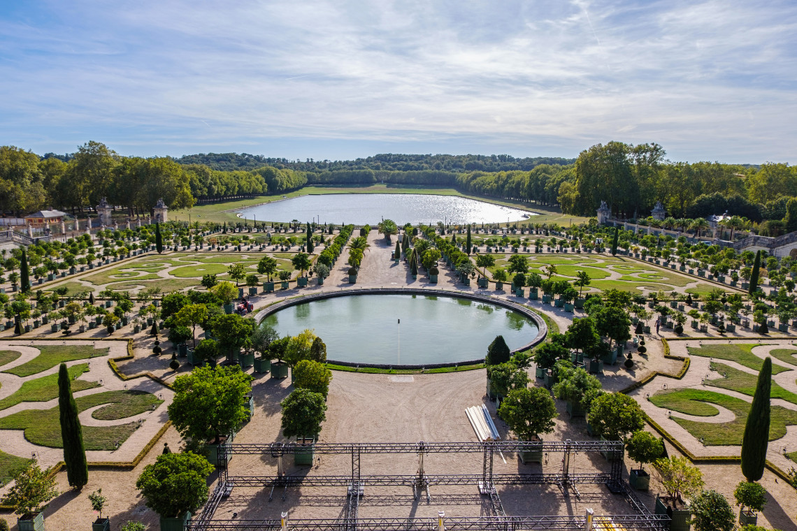 Aerial view of the Orangerie garden at the Palace of Versailles with a circular reflecting pool lined with manicured trees and the Swiss Lake visible beyond the formal parterre in France
