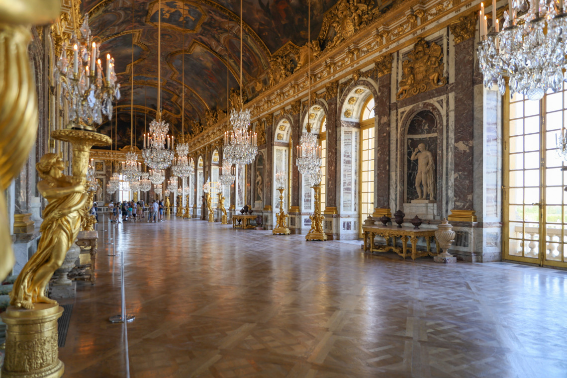The Hall of Mirrors at the Palace of Versailles with crystal chandeliers gilded statues painted ceilings and tall arched windows overlooking the gardens in France
