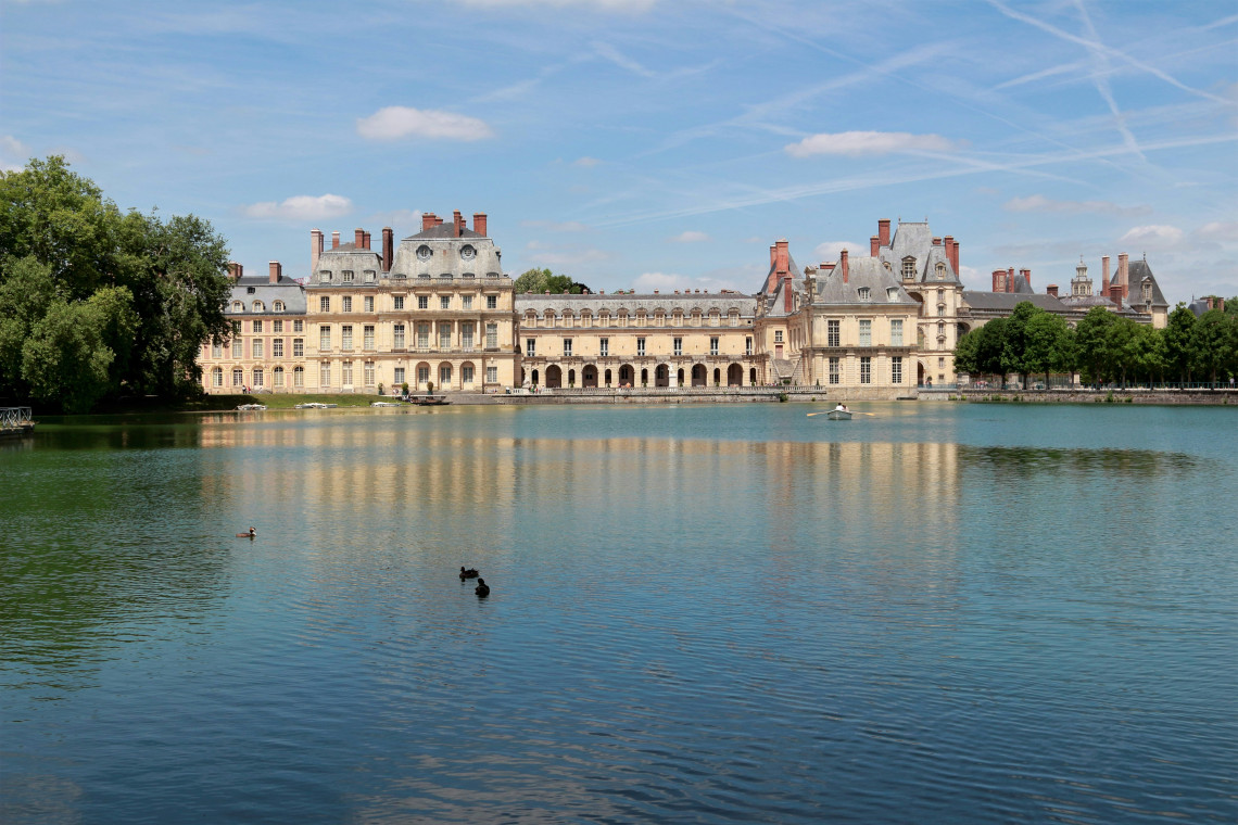 The facade of Chateau de Fontainebleau reflected in the still waters of the Carp Pond surrounded by parkland near Paris in Ile de France