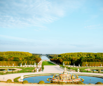 Aerial view of the formal gardens at the Palace of Versailles with an ornate fountain and the Grand Canal stretching into the distance in France