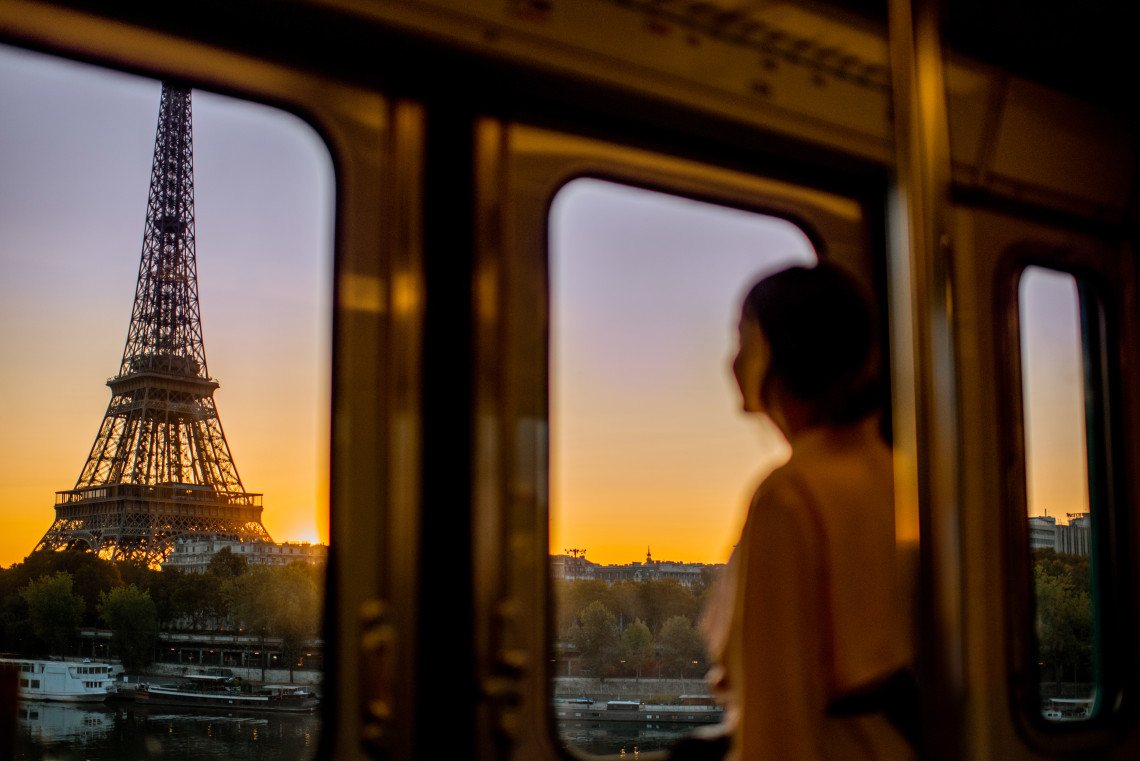 Woman looking at the Eiffel Tower at sunset through the window of a Seine River cruise boat in Paris, France