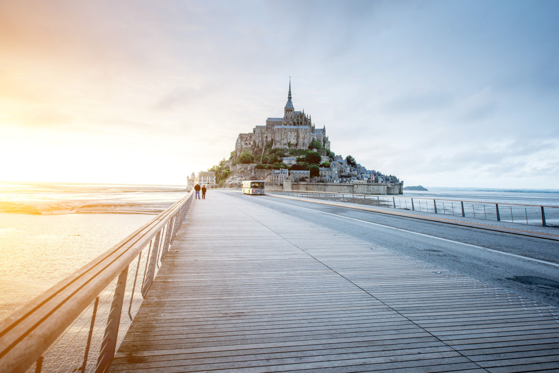 Wooden causeway leading to the medieval island abbey of Mont Saint-Michel at sunrise, Normandy, France