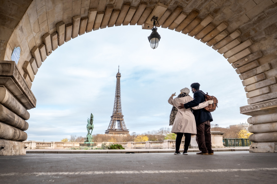 Couple embracing under the stone arch of Bir-Hakeim Bridge with the Eiffel Tower framed in the background, Paris, France