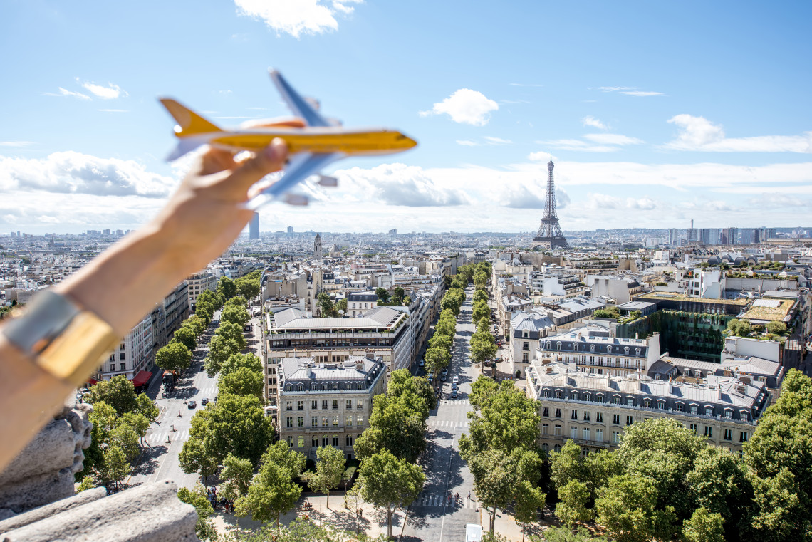 Hand holding a toy airplane over the Paris skyline with the Eiffel Tower and Champs-Elysees boulevards viewed from the Arc de Triomphe, France