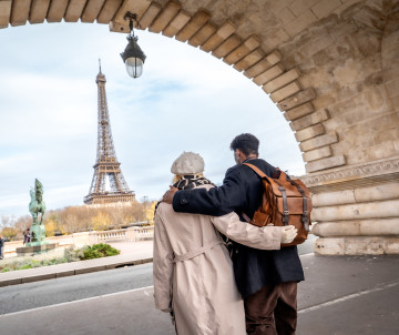 Couple embracing under the stone arch of Bir-Hakeim Bridge with the Eiffel Tower in the background, Paris, France