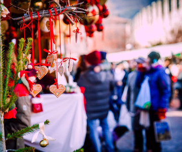 Handcrafted wooden and fabric ornaments hang from a decorated Christmas market stall in Budapest, Hungary. Shoppers in winter clothing appear softly blurred in the background.