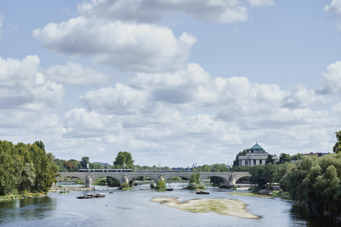 Stone bridge over the Loire River with green riverbanks and a domed building in the background, Loire Valley, France