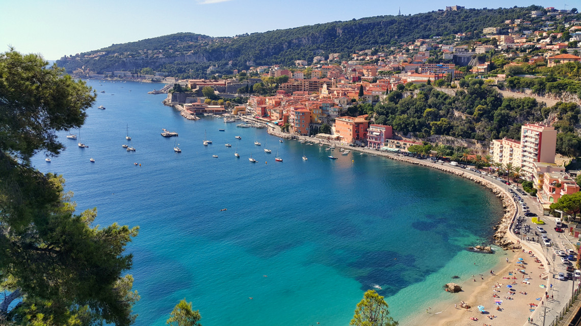 Aerial view of Villefranche-sur-Mer turquoise bay with sailboats, sandy beach and colorful hillside buildings on the French Riviera, France
