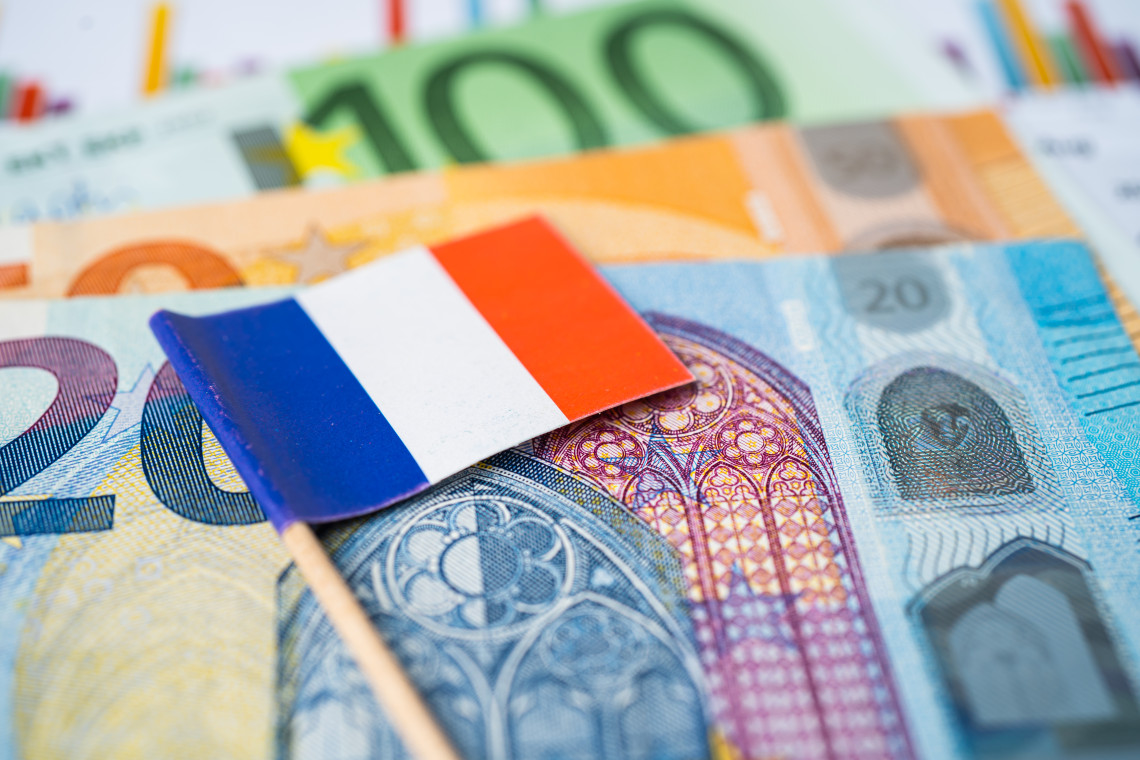 Small French flag placed on top of euro banknotes of various denominations, France travel budget concept