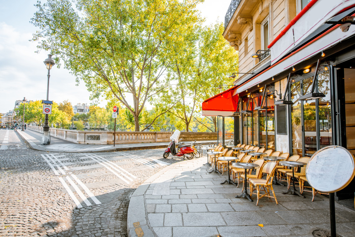 Traditional Parisian cafe terrace with wicker chairs and red awning on a cobblestone street near the Seine River, Paris, France