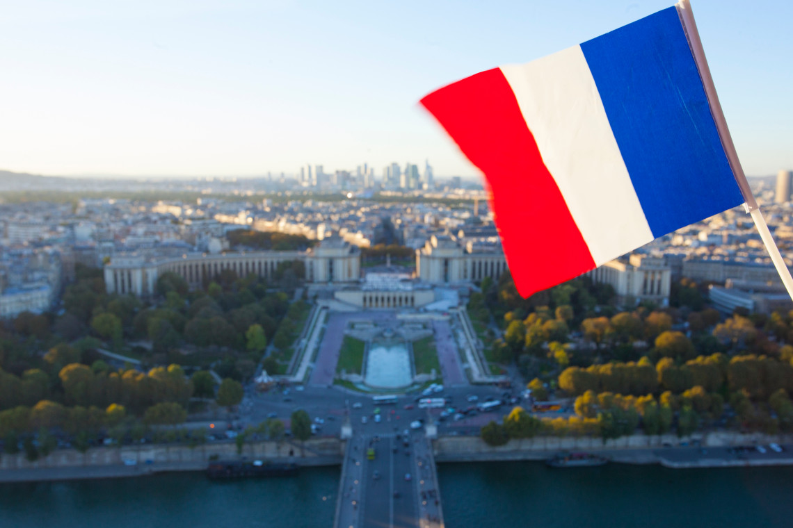 French flag in the foreground with aerial view of Trocadero gardens, Seine River and La Defense skyline from the Eiffel Tower, Paris, France