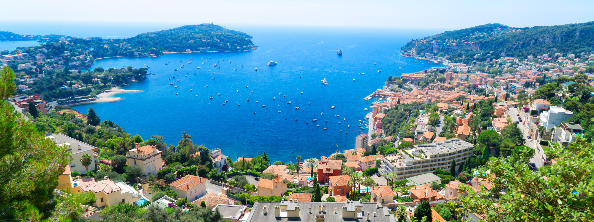 Panoramic aerial view of Villefranche-sur-Mer bay with sailboats, colorful hillside buildings and Cap Ferrat peninsula on the French Riviera, France