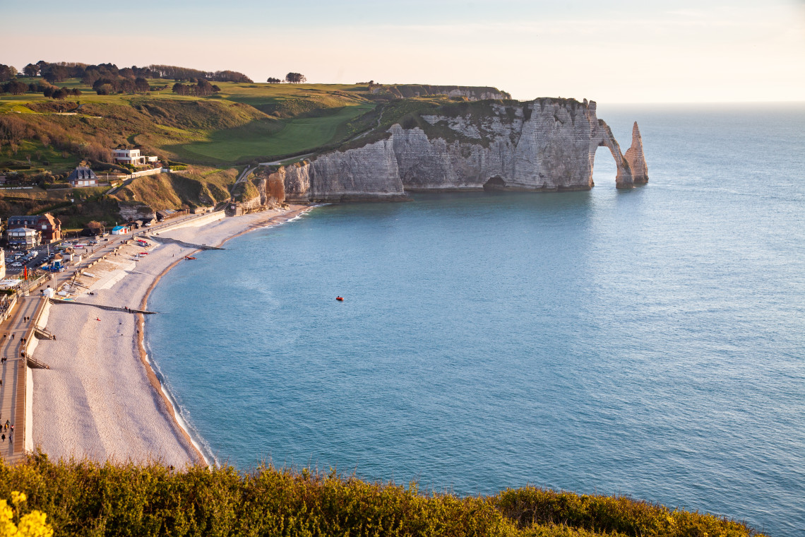 The iconic white chalk cliffs and natural rock arch at Etretat with the pebble beach and village below in Normandy France