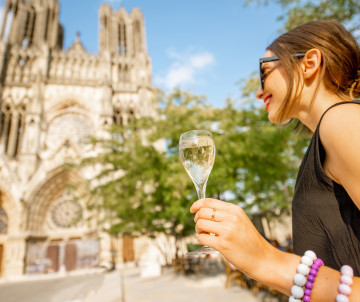 Woman holding a champagne flute in front of the Gothic Cathedral of Reims in the Champagne wine region, France