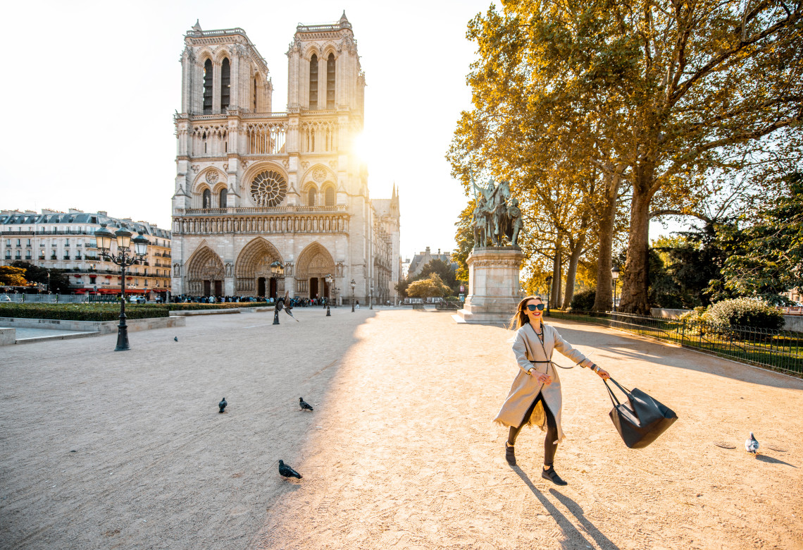 Stylish woman walking in front of Notre-Dame Cathedral at golden hour in Paris, France
