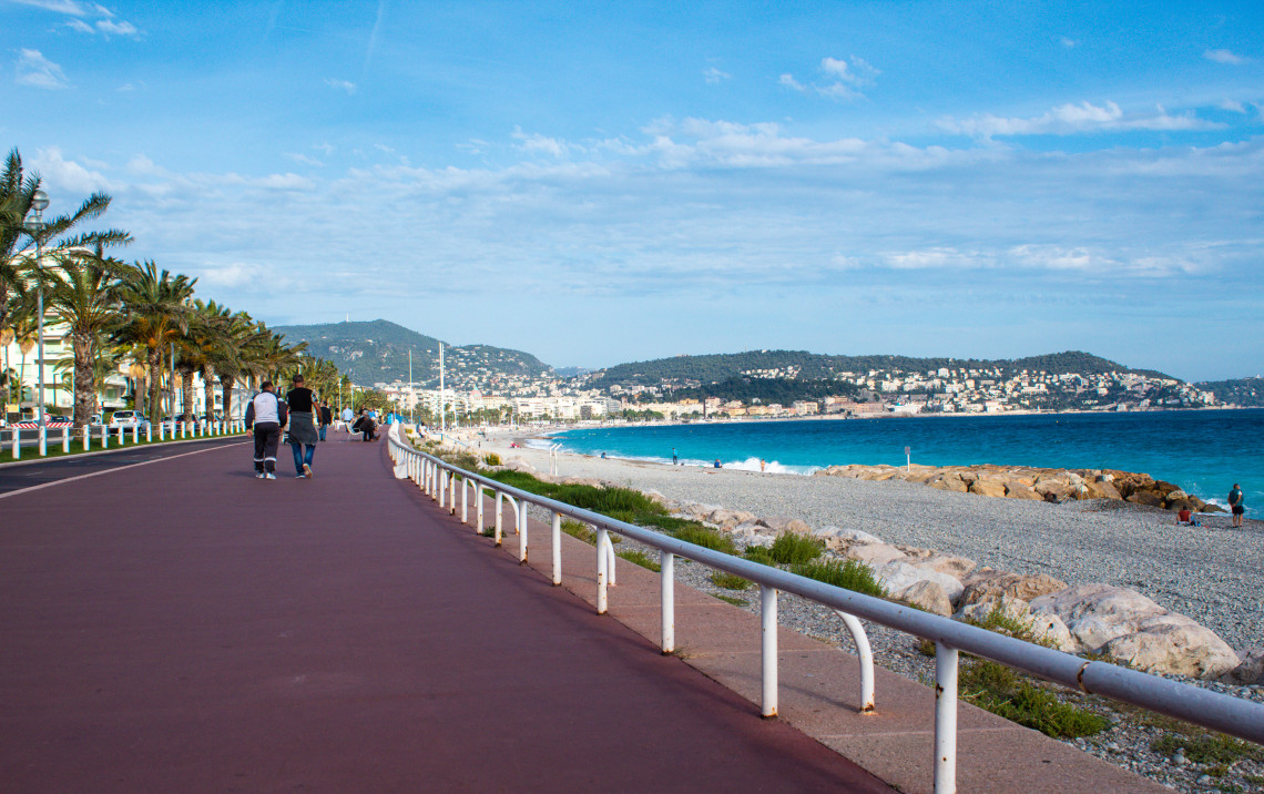  People walking along the Promenade des Anglais with pebble beach and turquoise Mediterranean Sea in Nice, Cote d'Azur, France