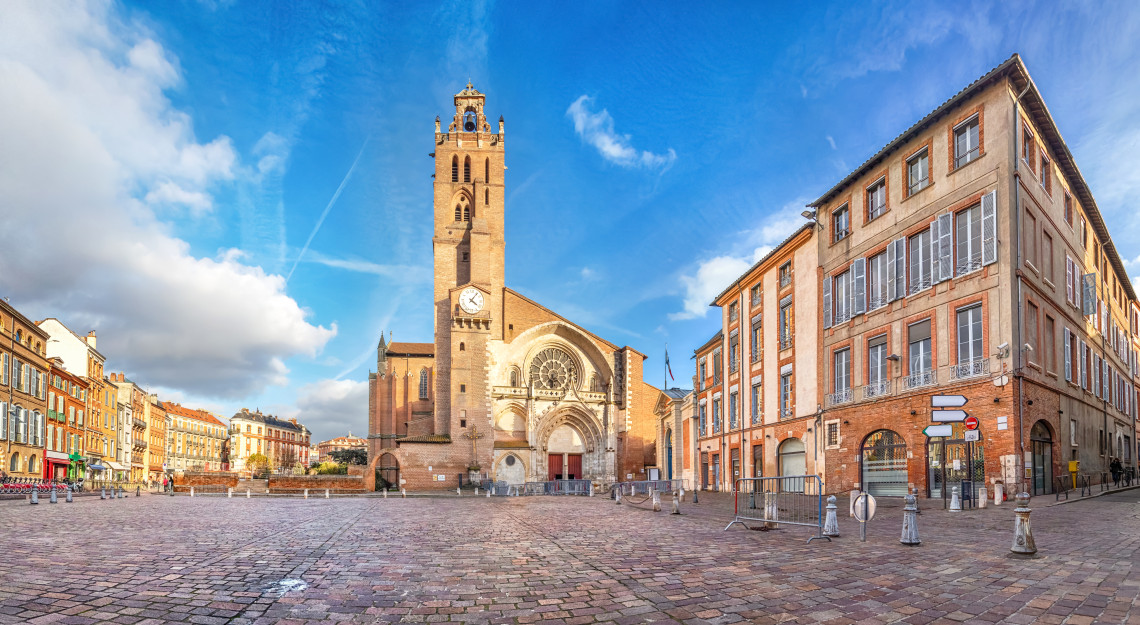 Panoramic view of Saint-Etienne Cathedral and cobblestone square surrounded by pink brick buildings in Toulouse, Occitanie, France