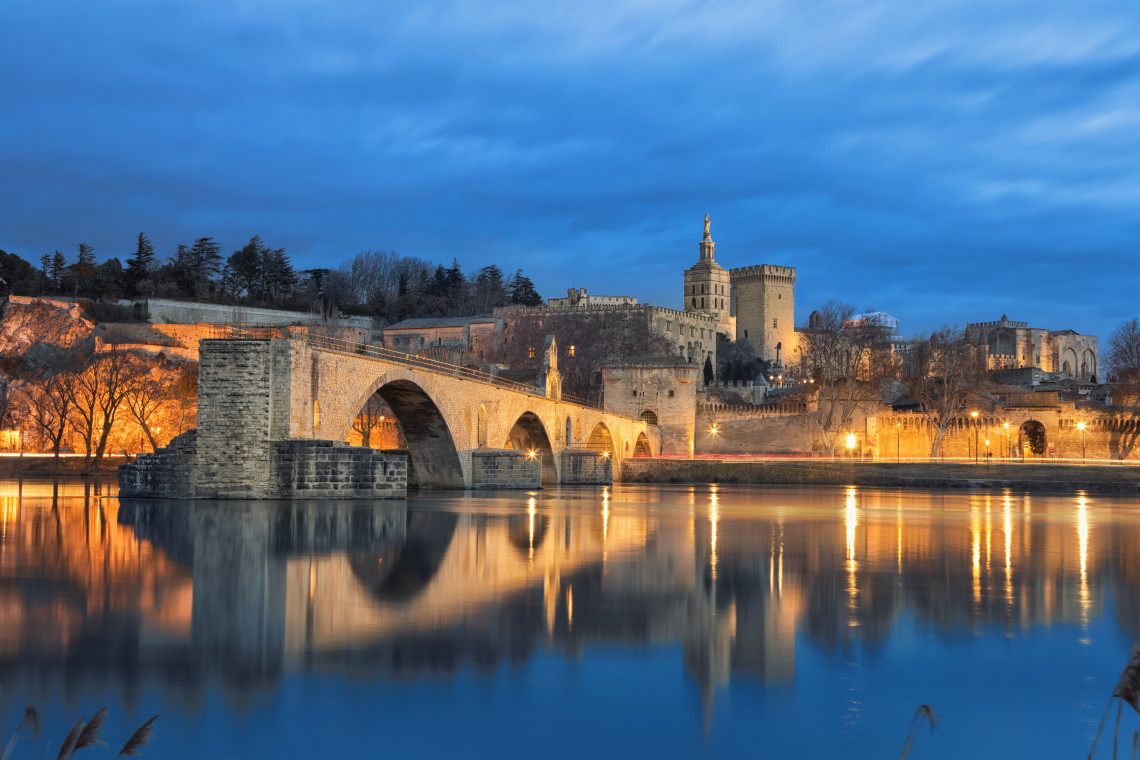 Pont Saint-Benezet bridge and illuminated Palais des Papes reflected in the Rhone River at dusk in Avignon, Provence, France