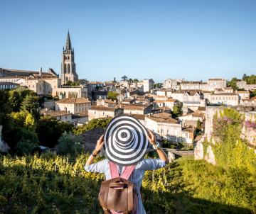 Woman with striped hat looking at the medieval village of Saint-Emilion with its church tower and vineyards in Bordeaux wine country, France
