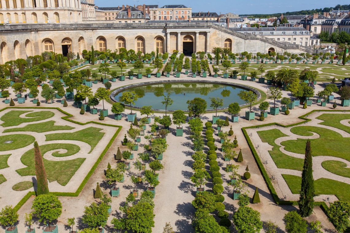Aerial view of the formal Orangerie gardens at the Palace of Versailles with geometric hedges, potted orange trees and circular fountain, near Paris, France