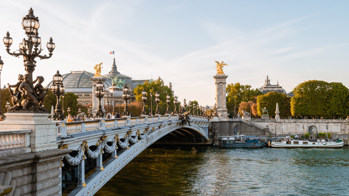 Ornate Pont Alexandre III bridge with golden statues and lamp posts over the Seine River with the Grand Palais in the background, Paris, France