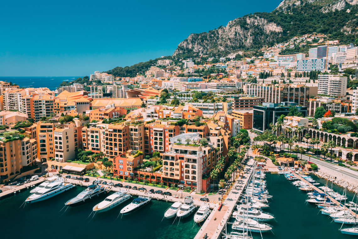 Aerial view of Monaco's Port de Fontvieille with luxury yachts, orange residential buildings and rocky hillside, Cote d'Azur