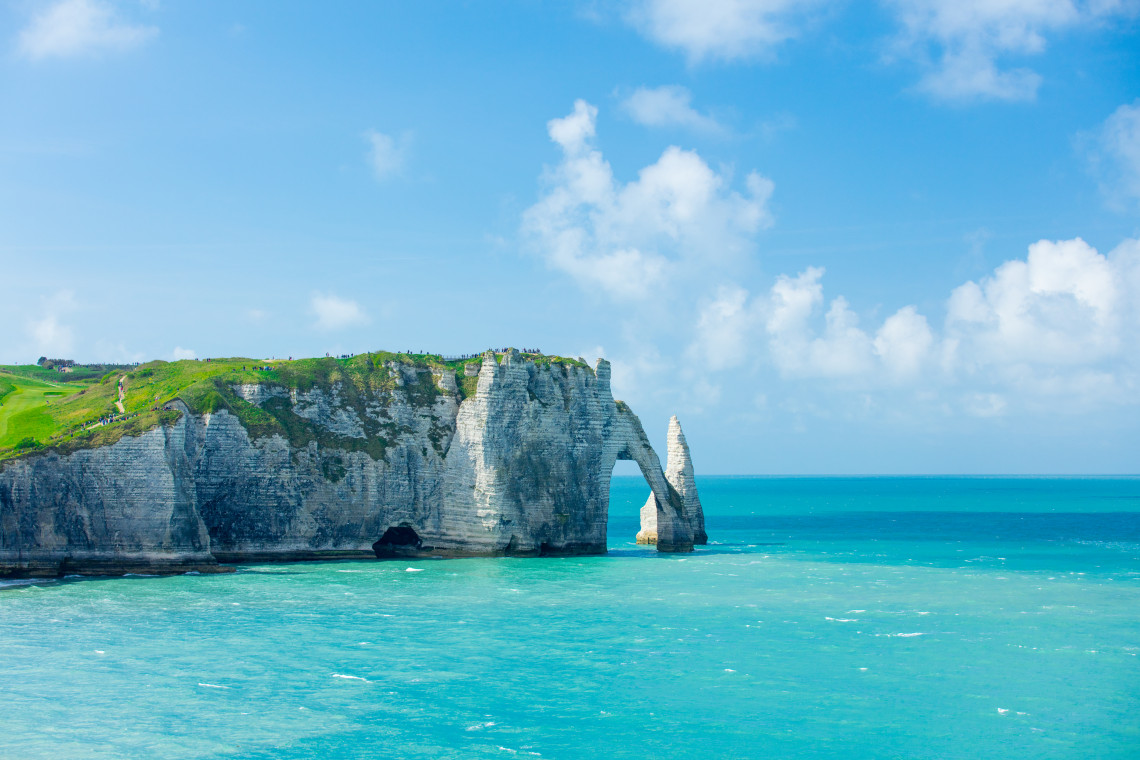 White chalk cliffs with natural arch and needle rock formation rising from turquoise water at Etretat, Normandy, France