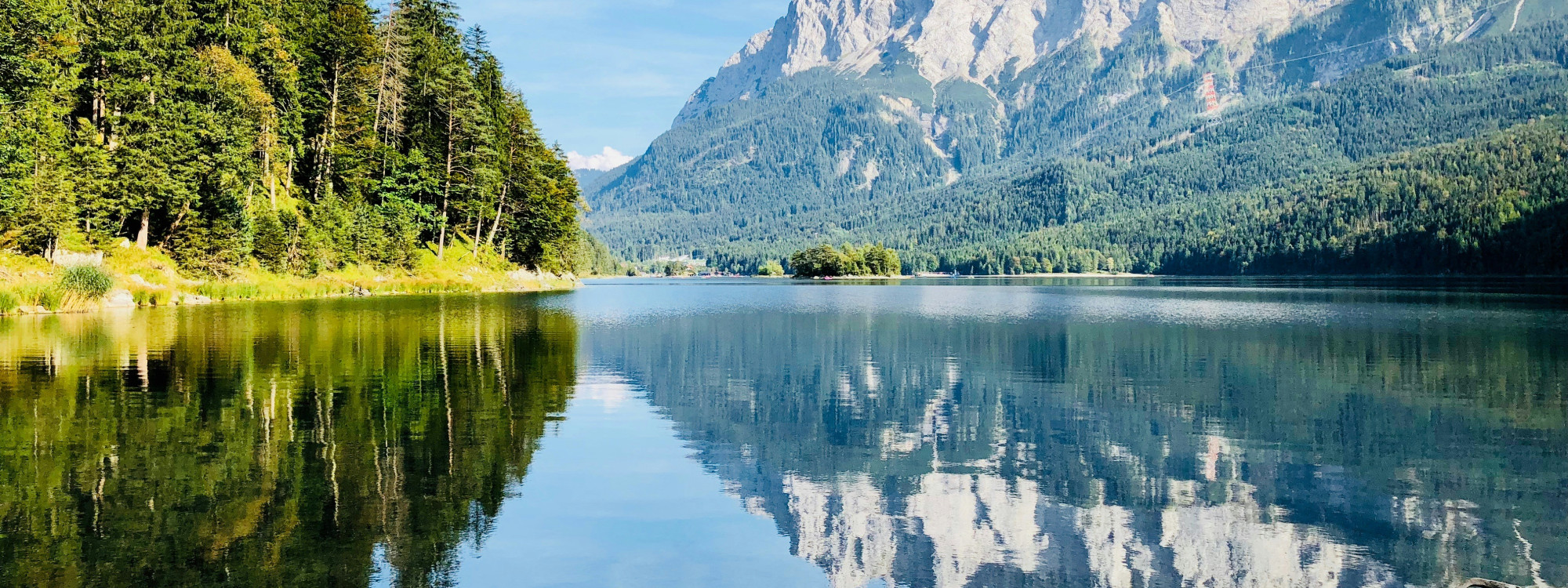 Calm waters of Hintersee reflect the surrounding forest and dramatic Bavarian Alpine mountains near Ramsau bei Berchtesgaden.