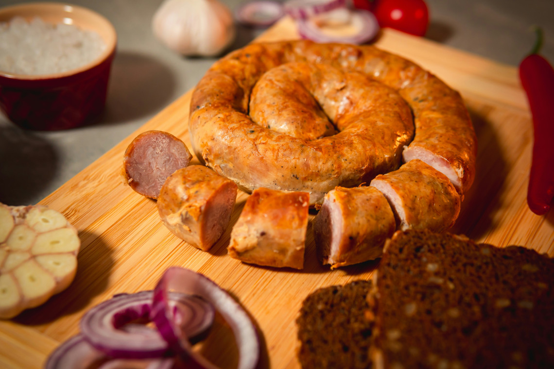 Coiled grilled bratwurst sausage served on a wooden board with bread, garlic and onions, representing traditional German cuisine.