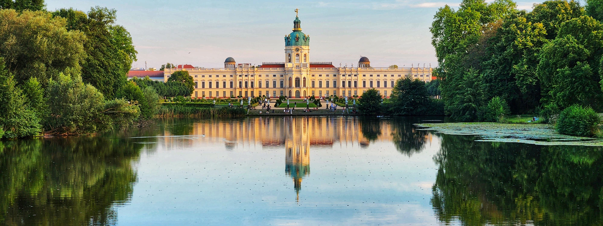 Charlottenburg Palace reflected in the calm water of its landscaped gardens, surrounded by mature trees in Berlin.