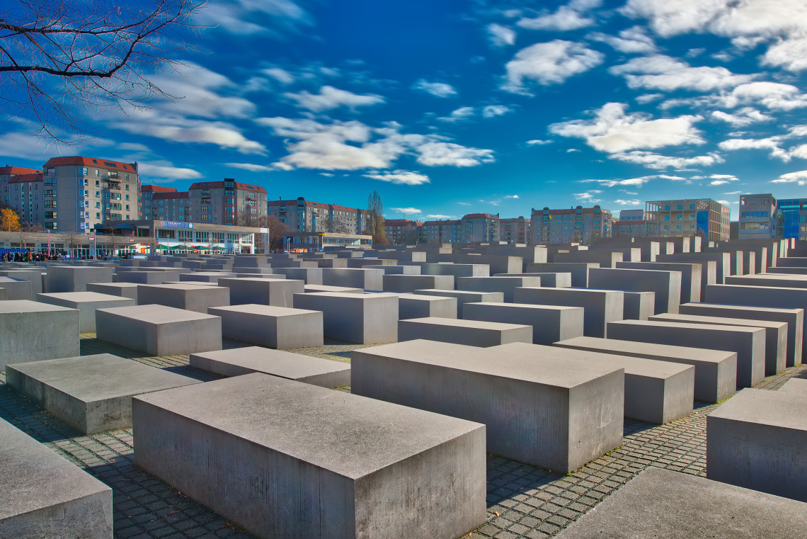 Rows of concrete stelae at the Memorial to the Murdered Jews of Europe in central Berlin beneath a dramatic blue sky.
