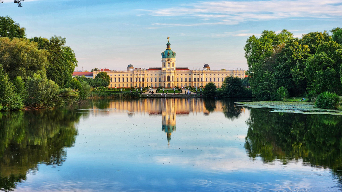Charlottenburg Palace viewed across a tranquil lake, with the historic palace and central tower reflected in the water.