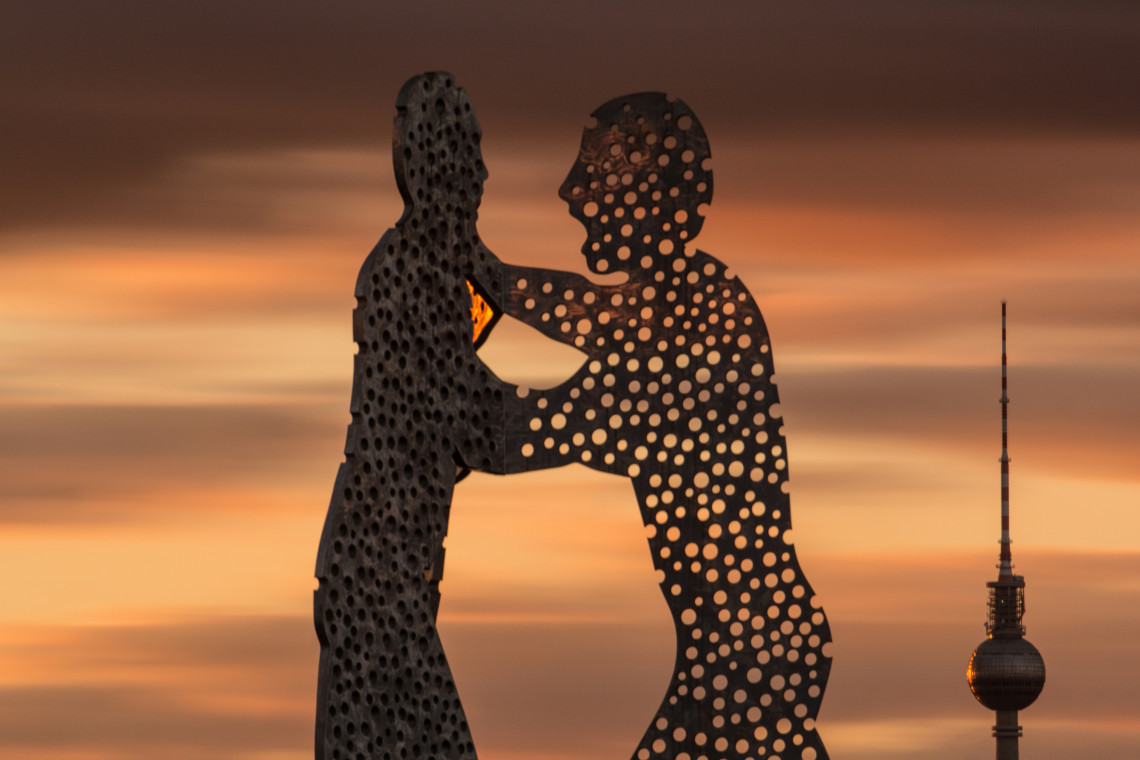 Silhouette of the perforated Molecule Man sculpture at sunset, with Berlin&rsquo;s Fernsehturm visible in the distance.