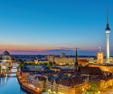 Panoramic view of central Berlin at sunset, with the Fernsehturm rising above the historic city center and the River Spree.